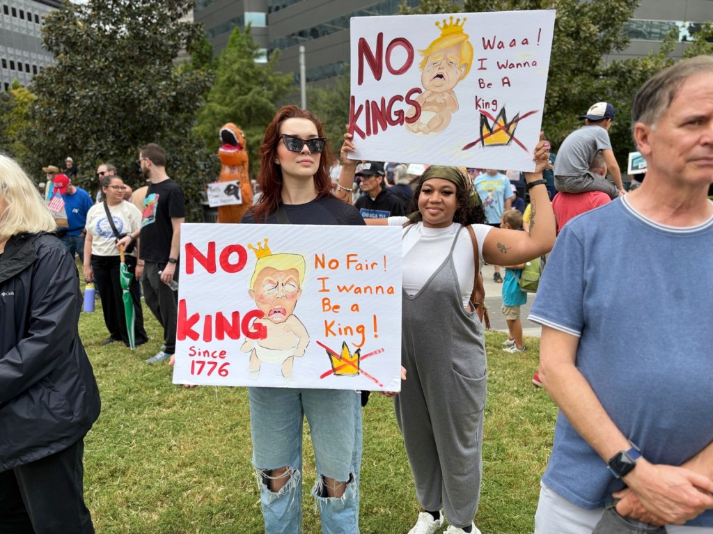 Protesters with signs depicting Donald Trump as both baby and king at Dallas protest.