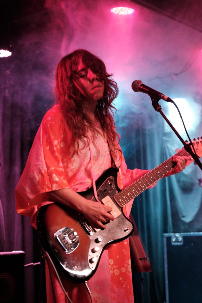 Claire Morales, a musician and visual artist, plays guitar on stage.