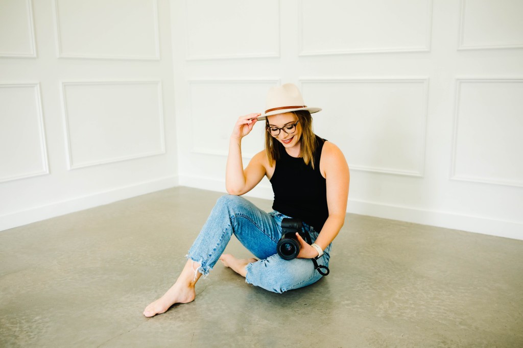 Photobrapher Taylor Rollins sits barefoot on a floor with her camera.