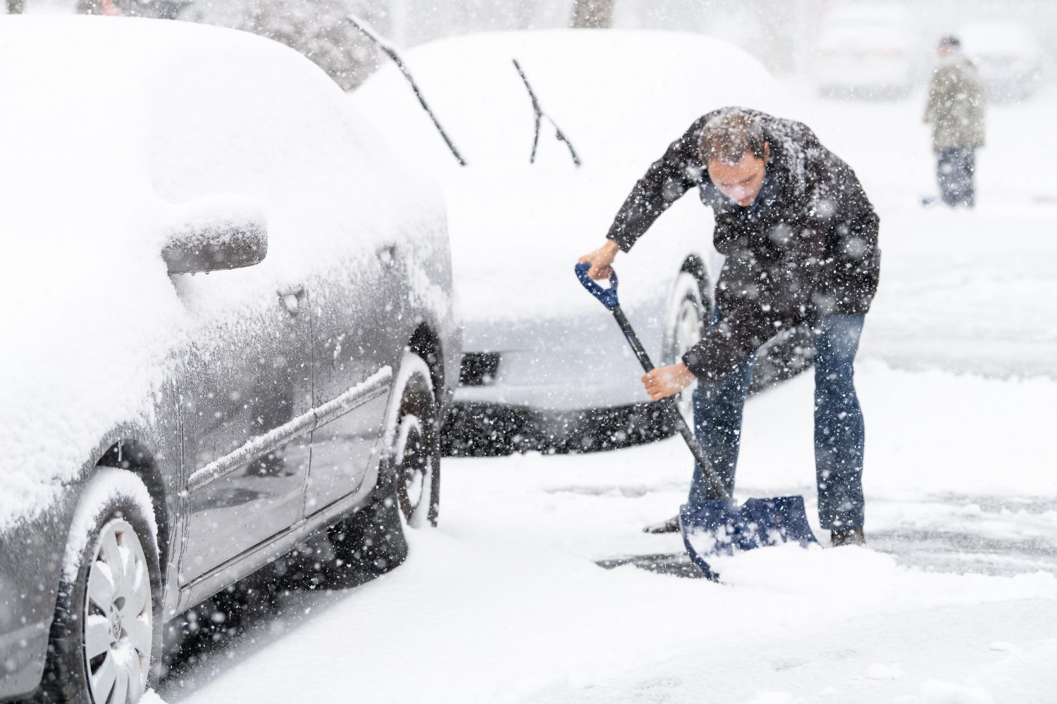 man shoveling snow next to car
