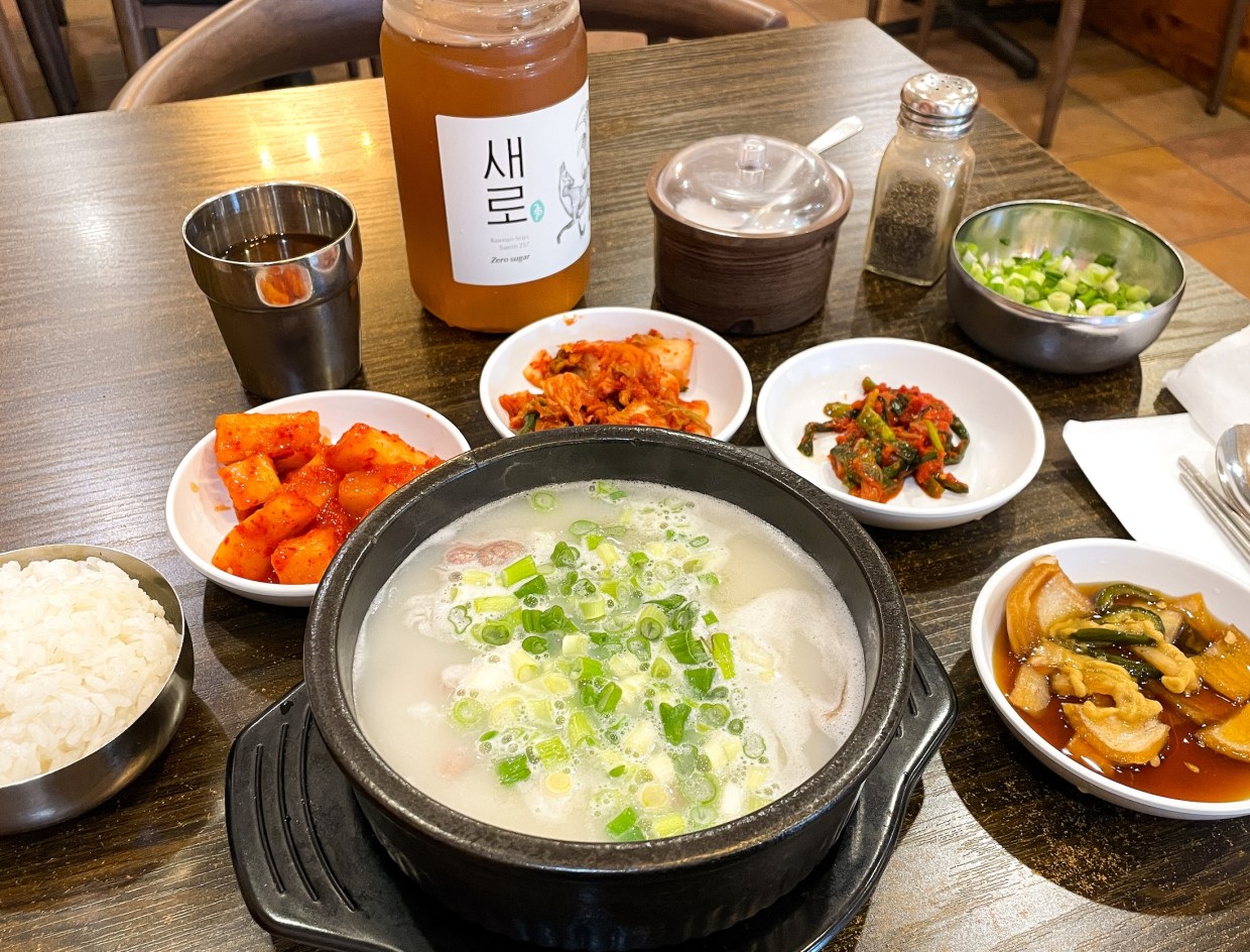 Doma Seolleongtang soup and all the sides sitting on a brown table.