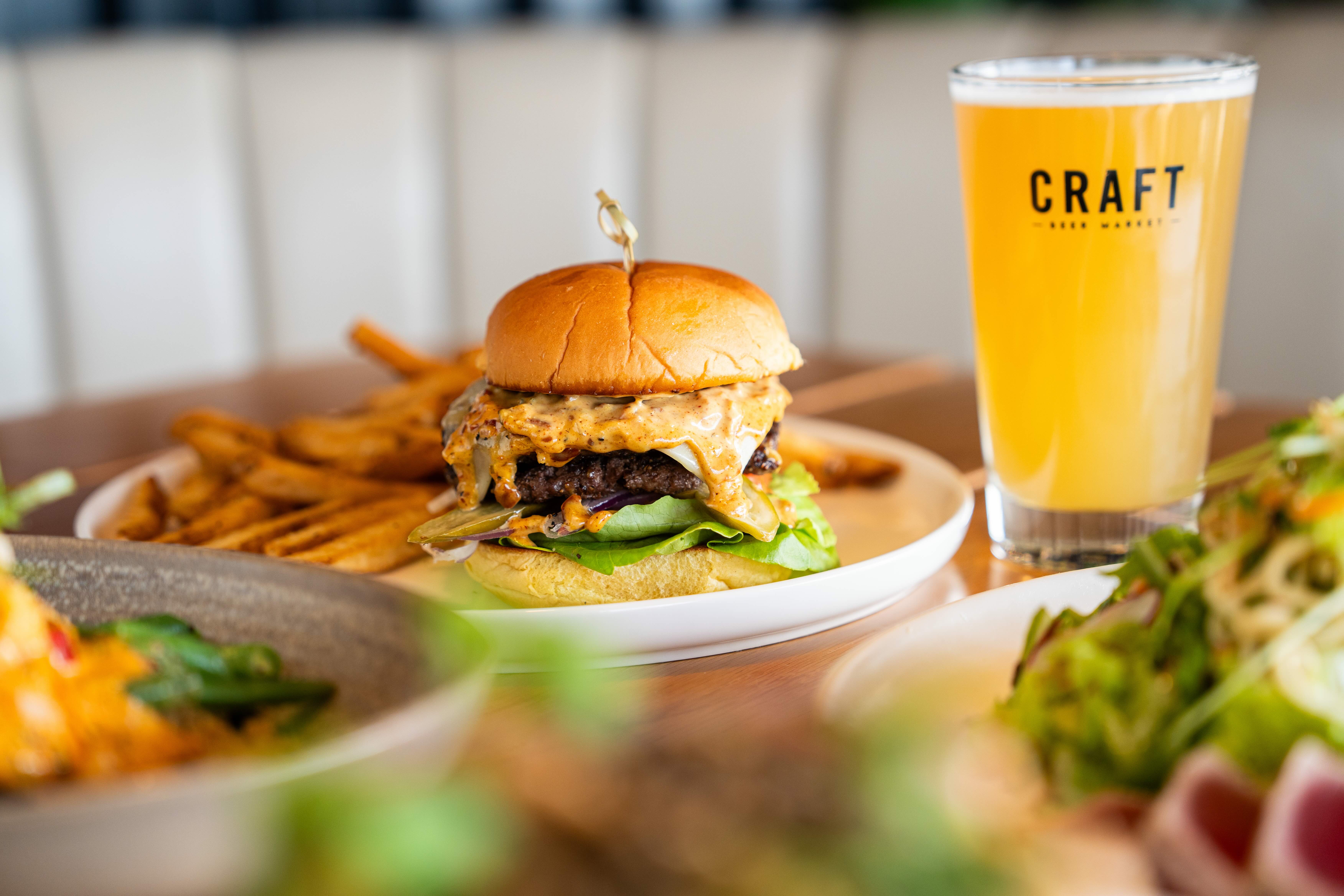 A large burger oozing with cheese and a beer.
