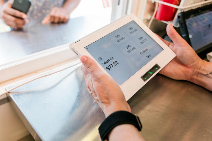 A close-up view of a transaction at the "Hogs and Hops" BBQ event, showcasing the modern payment process. The payment screen displays tipping options while a customer interacts with the staff. The image emphasizes the blend of technology and customer service, reflecting the seamless and efficient transaction experience at the event.