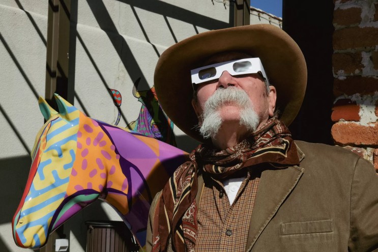 A cowboy stares at the sky wearing eclipse glasses.