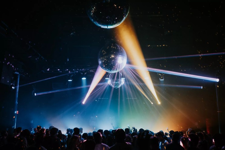 A crowd dances at a rave under disco balls.